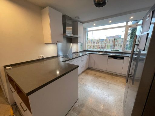 Moderne keuken met grijs aanrecht, witte kasten en grote ramen voor natuurlijk licht.